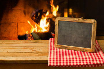 Chalkboard on wooden table over fireplace background. Winter and Christmas holiday concept