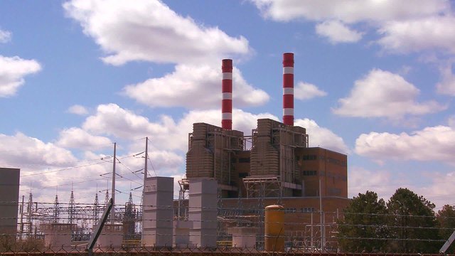 A power plant with striped towers with clouds moving behind.