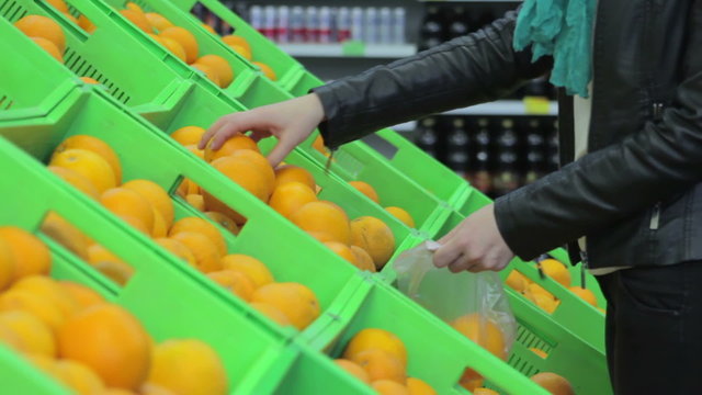Young woman in supermarket. Buyer picks oranges out of the box close-up