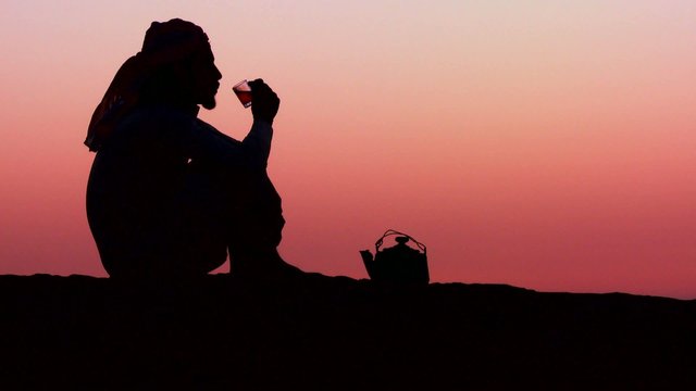 A Bedouin man pours tea in silhouette against the sunset.