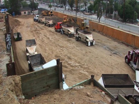 A back hoe dumps a load of dirt into the trailer of a semi.