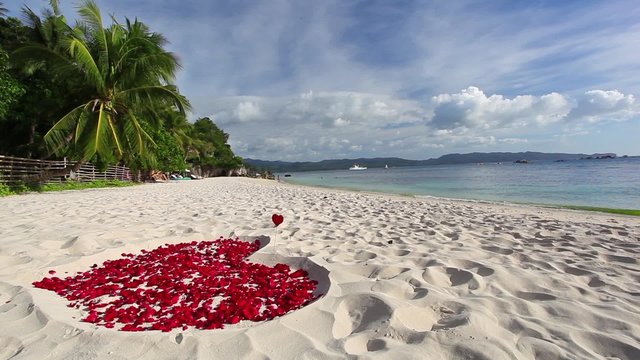 Heart of roses petals on tropical sandy beach. Nobody. Love concept
