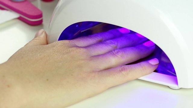 Manicure in process - putting hand and curing gel varnish in nail LED lamp, procedure of polymerization