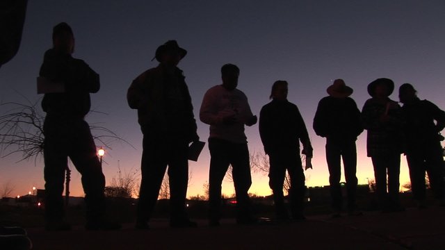 In the early morning hours, seven or eight men are standing around holding papers and waiting.