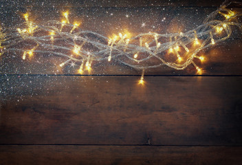 Christmas warm gold garland lights on wooden rustic background. filtered image with glitter overlay