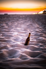 Beer bottle in the sand as the sunsets at the beach