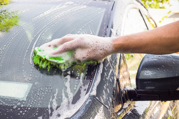 Mans hand washing car with sponge and suds