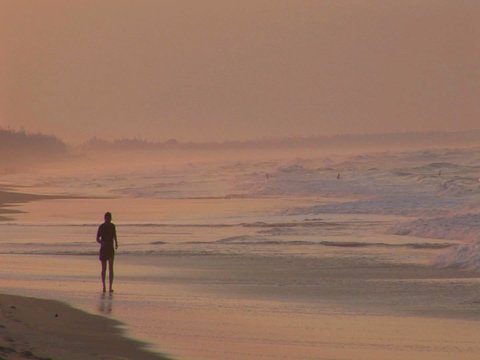 A man jogs along a beach in silhouette.