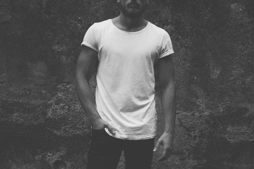 black and white photo. blank white t-shirt on muscle young man, dark concrete background