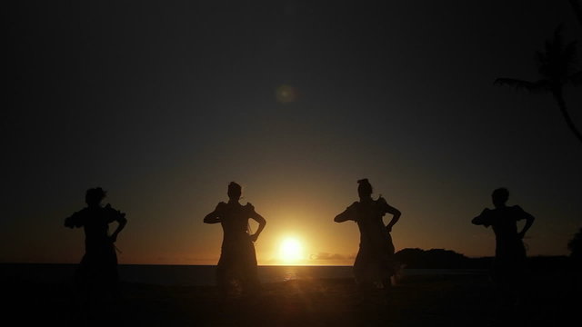 Native Hawaiian dancers perform in the distance at sunset.