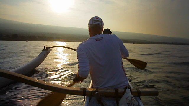 Slow motion of kayaks or outriggers rowing into sunset.