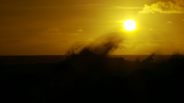 The sunset behind waves as they crest and break in slow motion at sunset.