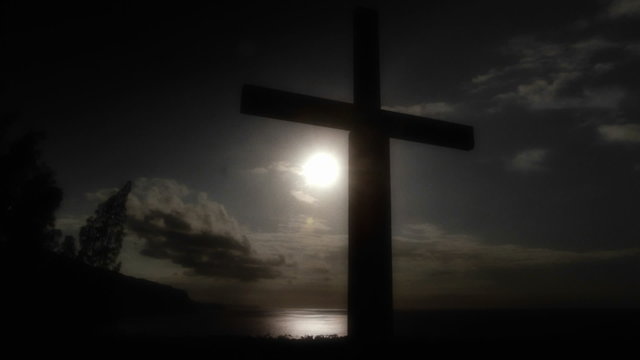 Pan across to a Christian cross against the sun on a cloud, moody day.