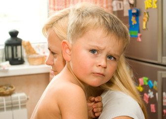 Sad boy on a mom's hands in a kitchen on a fridge with magnets background - 91781181