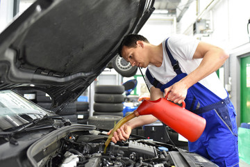 Fototapeta na wymiar Mechaniker füllt Motoröl im Auto in einer Werkstatt nach // oil change in a car workshop - garage