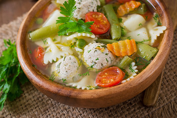 Diet vegetable soup with chicken meatballs and fresh herbs in wooden bowl