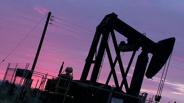 An oil derrick pumps against a purple sky.