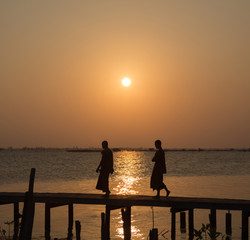 Monks crossing the bridge at sunset on lake,Thailand