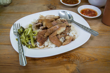 Stewed pork leg on rice with side bowl on wooden table.Thai food