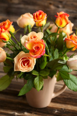 Bouquet of orange roses in cup on brown wooden background