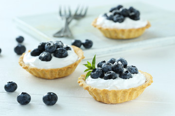 Dessert tartlets with blueberries on white wooden background