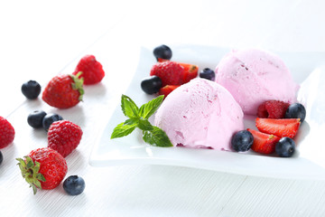 Ice cream on plate with berries on white wooden background
