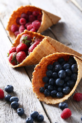 Waffle cones with berries on wooden table