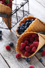 Waffle cones with berries on wooden table