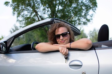 Beautiful young woman in a convertible car, with car key in hand. 
