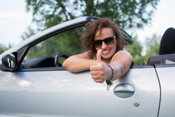 Beautiful young woman in white shirt and black glasses, smiling and gives thumb up from a car