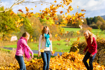 Mädchen haben Spaß und werfen mit Herbst Laub im Park