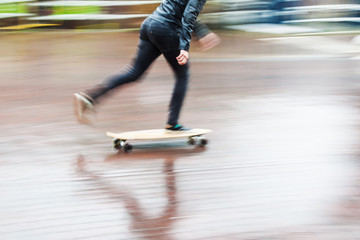 Fototapeta na wymiar Skateboarder auf nasser Straße in Bewegungsunschärfe