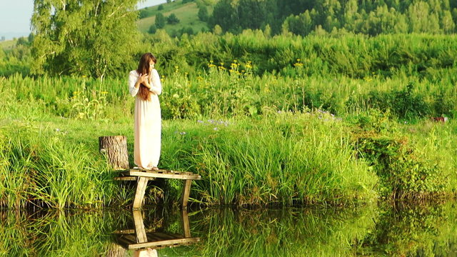 Pretty girl in a long dress poses near a scenic lake
