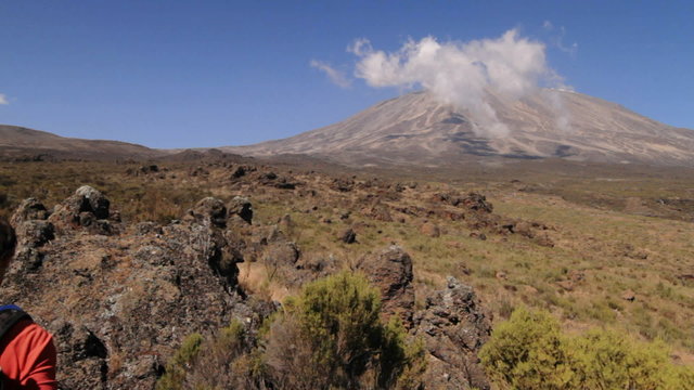 Wide shot of Kilimanjaro with trekker walking into frame