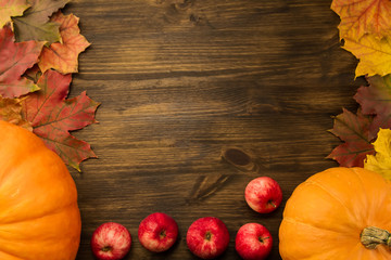 Yellow ripe pumpkin, maple leaves, red apples on wooden background. Thanksgiving, autumn.