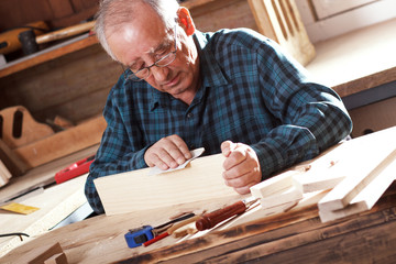 Senior carpenter sanding plank in his workshop