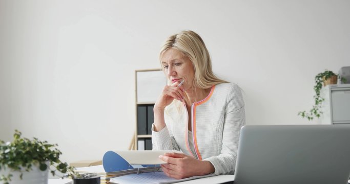erfolgreiche unternehmerin sitzt am schreibtisch und bl&auml;ttert in unterlagen