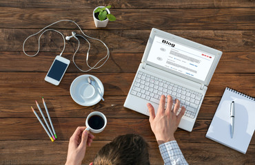 Writer Working on Computer at Wooden Desk Top View of Man Typing on Laptop and Holding Coffee Mug at Warm Natural Wood Table with Electronic Gadgets and Stationery Tools for Every Day Life