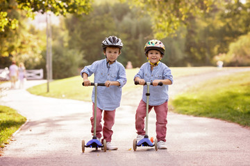 Two cute boys, compete in riding scooters, outdoor in the park,