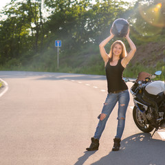 Blonde girl removes his helmet near motorcycle.