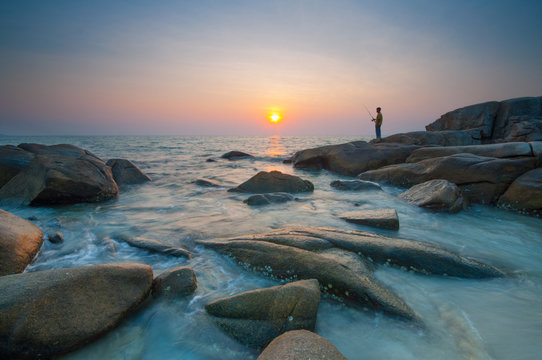 Fisherman on rock while sunset
