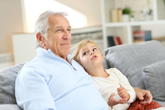 Portrait of grandfather with little girl sitting in couch
