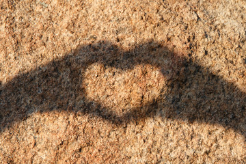 Hand of heart-shaped shadow on stone