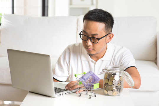 asian guy using internet computer and counting coins at home. As