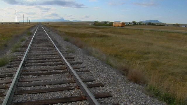 A school bus passes an old railroad track that lays across a prairie.