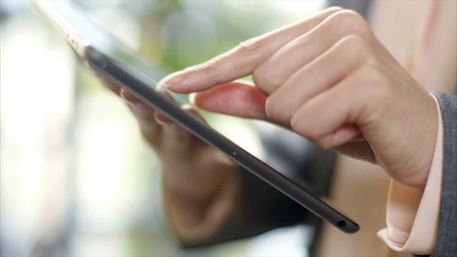 Cropped video of businesswoman's hands using tablet computer. Female professional is scrolling and zooming. She is in brightly lit office.
