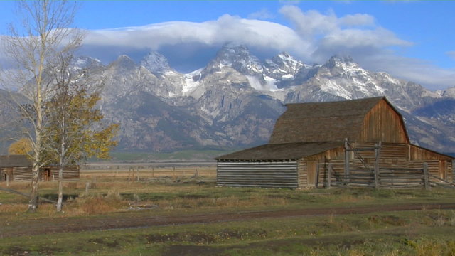 An old barn stands with the Grand Teton mountains in the background.