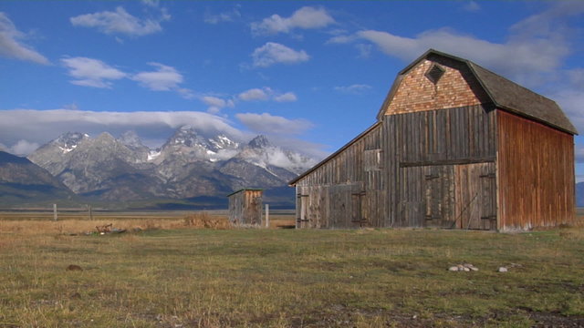 An old barn sits in a field with the Grand Teton mountain Range in the background