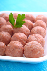 meat balls from raw minced meat in a white tray on a blue background