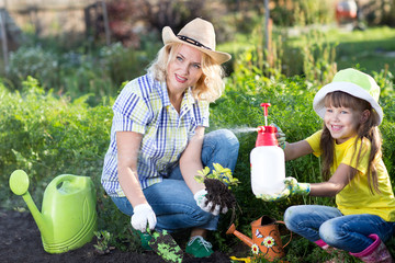 Happy woman and kid girl on farm garden in summer, planting